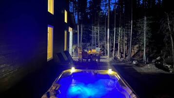 A hot tub in a forested area with a dining table and chairs, surrounded by tall trees.