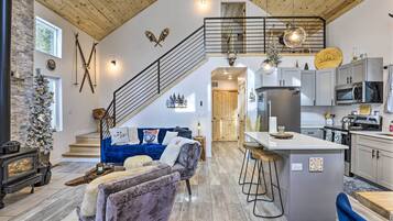 A spacious living area with a fireplace, a blue sofa, a wooden staircase, and a kitchen with modern appliances.