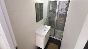 Casa de banho com lavatório branco, espelho e cabine de duche em vidro.
