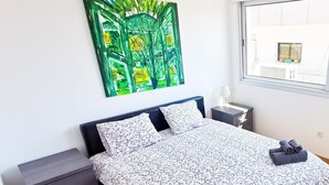 Quarto com cama, mesa de cabeceira, luminária e janela com vista para o exterior.