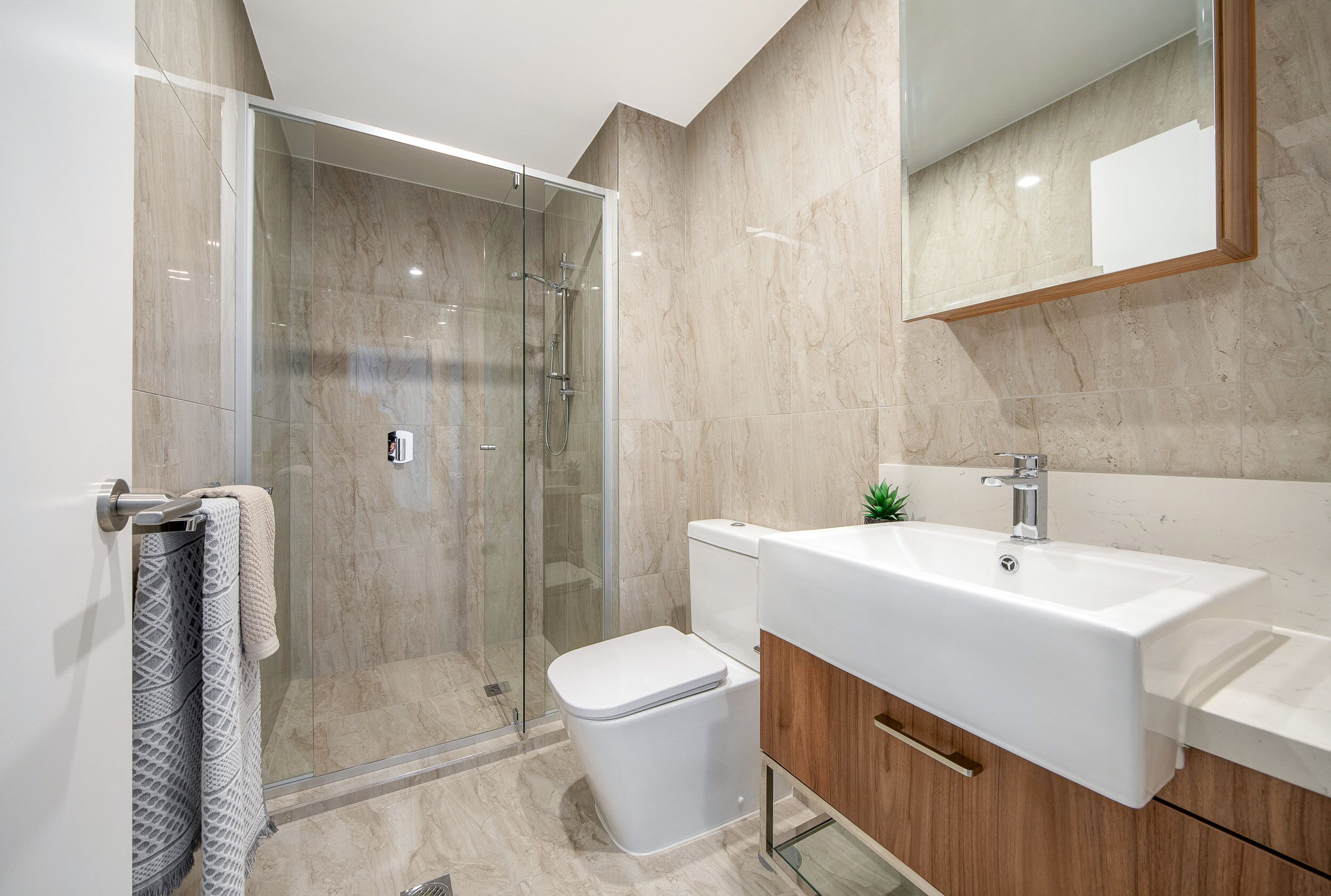 A modern bathroom with a glass shower enclosure, a white toilet, and a wooden vanity with a sink.