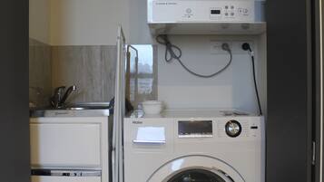 Un área de lavandería compacta con lavadora y secadora apiladas, un refrigerador pequeño y un calentador de agua.