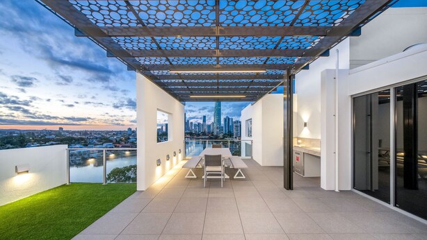 A rooftop terrace with a dining table and chairs, a pergola with a patterned ceiling, and a city view.