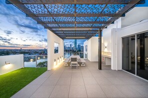 A rooftop terrace with a dining table and chairs, a pergola with a patterned ceiling, and a city view. - Serenity Surfers Paradise (Surfers Paradise)