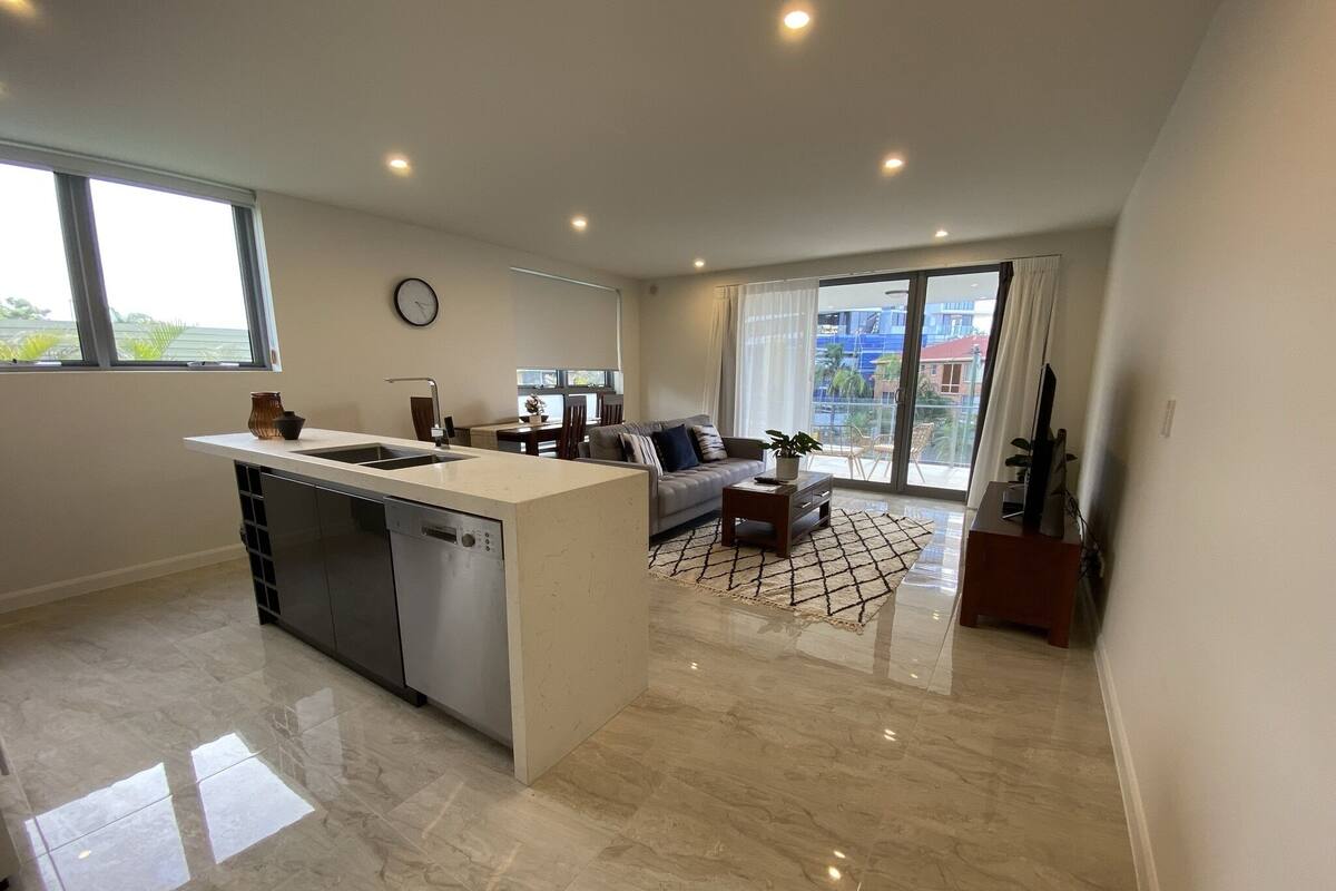 A modern kitchen with a dishwasher, a dining area with a sofa and a coffee table, and a living room with a sofa and a TV.