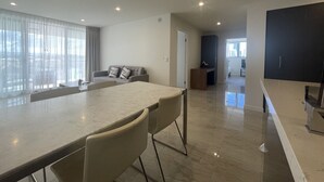 A modern living room with a large dining table, a sofa, and a kitchen area with a dark cabinet.