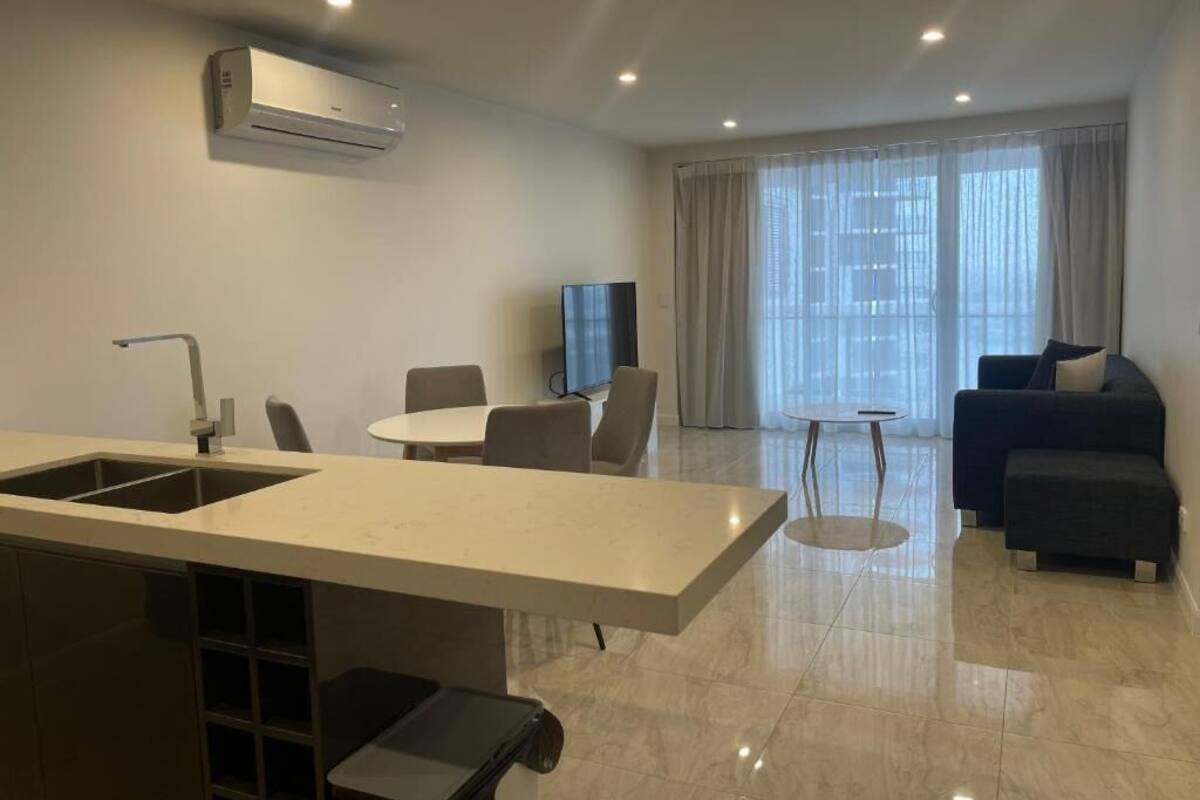 A modern living room with a kitchen area, a dining table, and a sofa.
