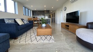 A spacious living room with a blue sofa, a wooden coffee table, and a large flat-screen TV.