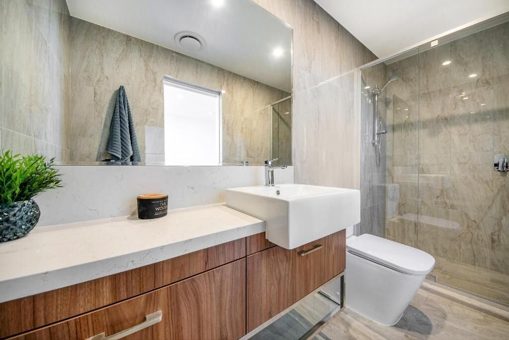 A modern bathroom with a marble vanity, a glass shower enclosure, and a toilet.