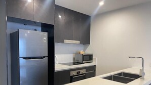 A modern kitchen with dark cabinets, a stainless steel refrigerator, a microwave, and a white countertop.