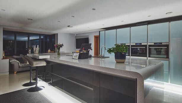 Cocina moderna con una isla grande, hornos empotrados y un mamparo de vidrio.