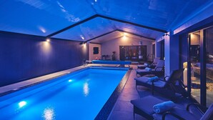 Una piscina interior con techo de cristal, sillones de descanso y equipo de ejercicio.