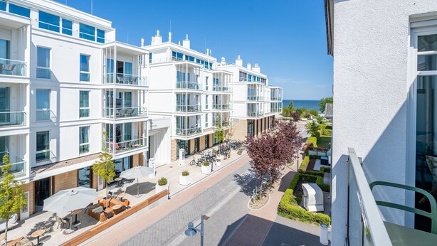 A modern hotel with multiple floors, outdoor seating areas, and a view of the sea.
