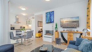 A modern living room with a fireplace, a dining area, and a kitchen in the background.
