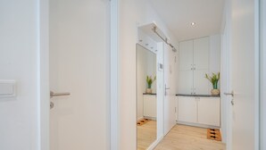 A hallway leading to a kitchen with white cabinets, a wooden floor, and a mirror reflecting the space.