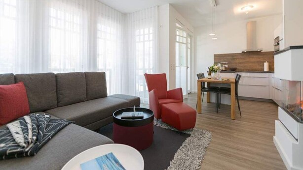 A modern living room with a sofa, red chair, and a dining area with a table and chairs.