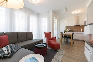 A modern living room with a sofa, red chair, and a dining area with a table and chairs.