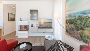A modern living room with a fireplace, a large painting, and a view of the ocean.
