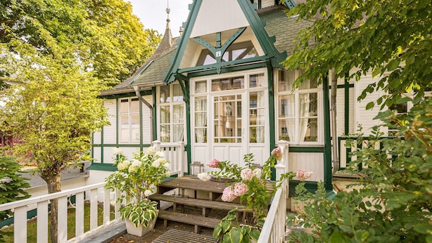 A traditional house with a green and white exterior, a wooden staircase leading to a porch, and potted plants. - Vacation home Strandschlösschen (Heringsdorf)