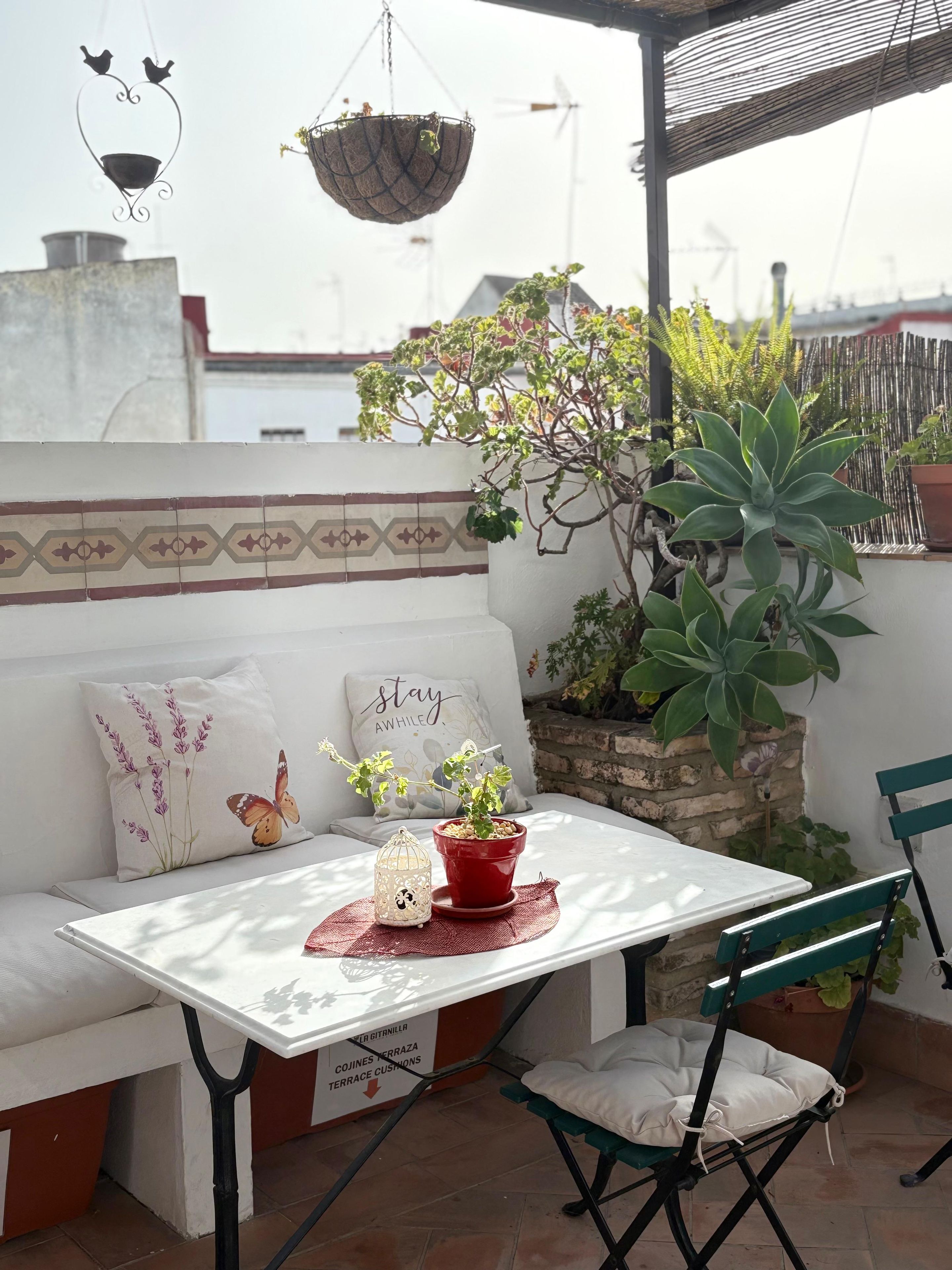 A patio with a white table, green chairs, a red potted plant, and a hanging basket.
