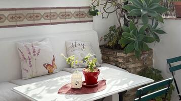 A patio with a white table, green chairs, a red potted plant, and a hanging basket.