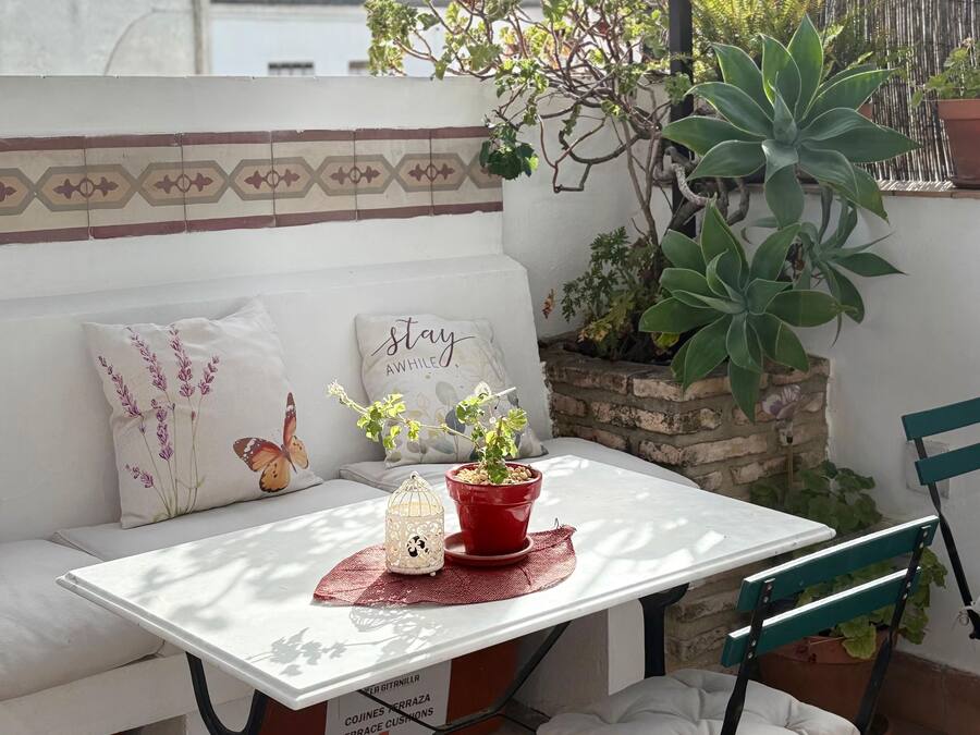 A patio with a white table, green chairs, a red potted plant, and a hanging basket.