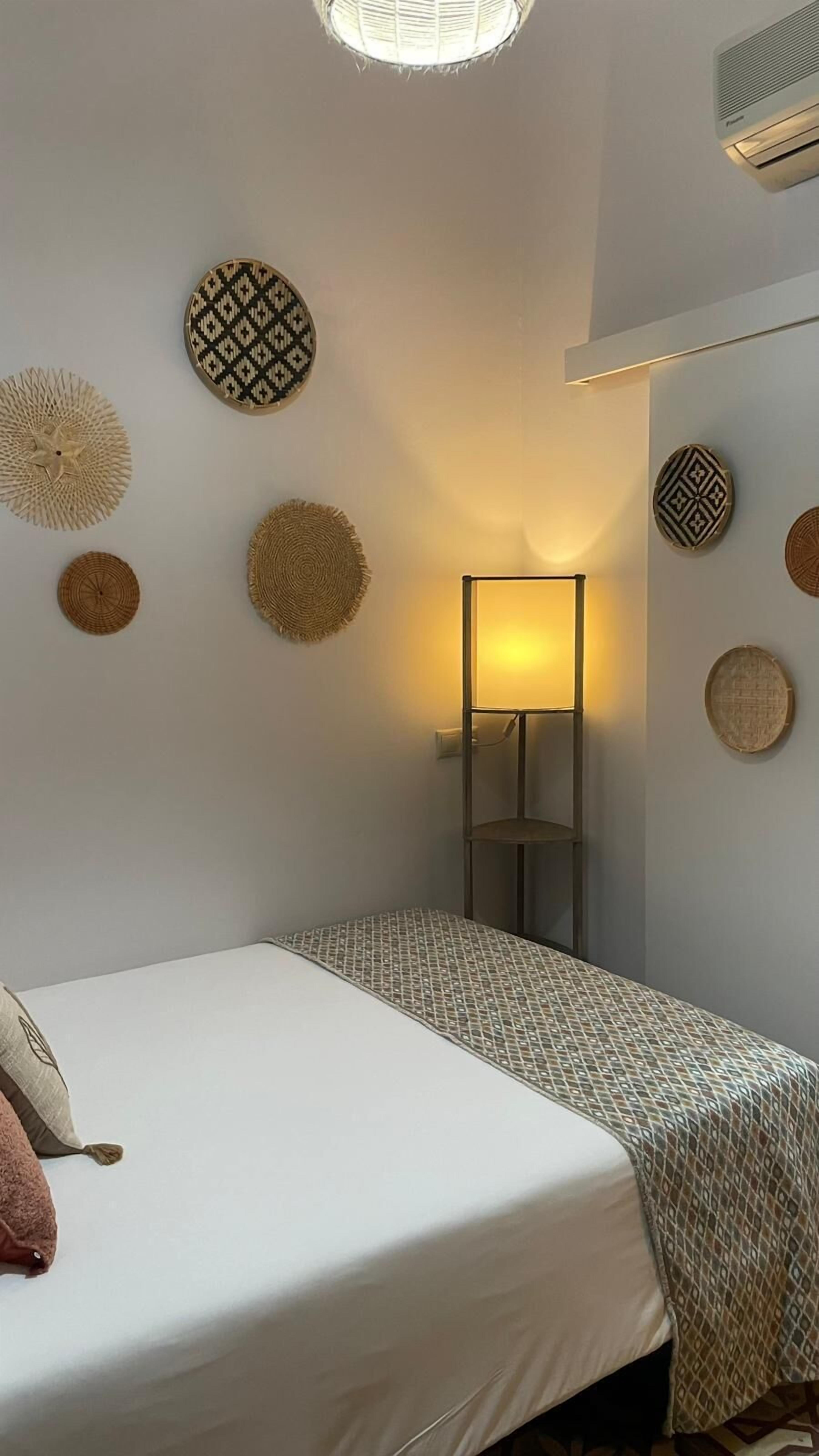 A bedroom with a bed, a bedside lamp, and decorative wall hangings.