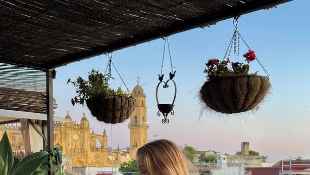 A woman standing by a table with potted plants and a hanging basket. - La Gitanilla Alojamiento & Encanto (Jerez de la Frontera)