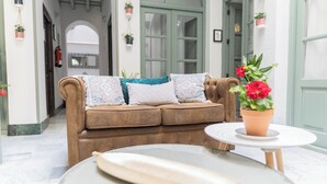 A cozy seating area with a brown sofa, patterned cushions, and a small round table with a potted plant. - La Gitanilla Alojamiento & Encanto (Jerez de la Frontera)