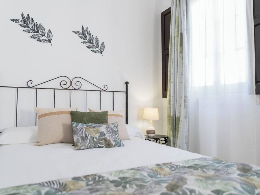 Un letto rifatto con cura, una coperta a fiori, una lampada da comodino e due quadri appesi al muro.