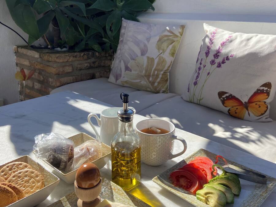 A table set with food and drinks on a terrace with a view of a building and plants.