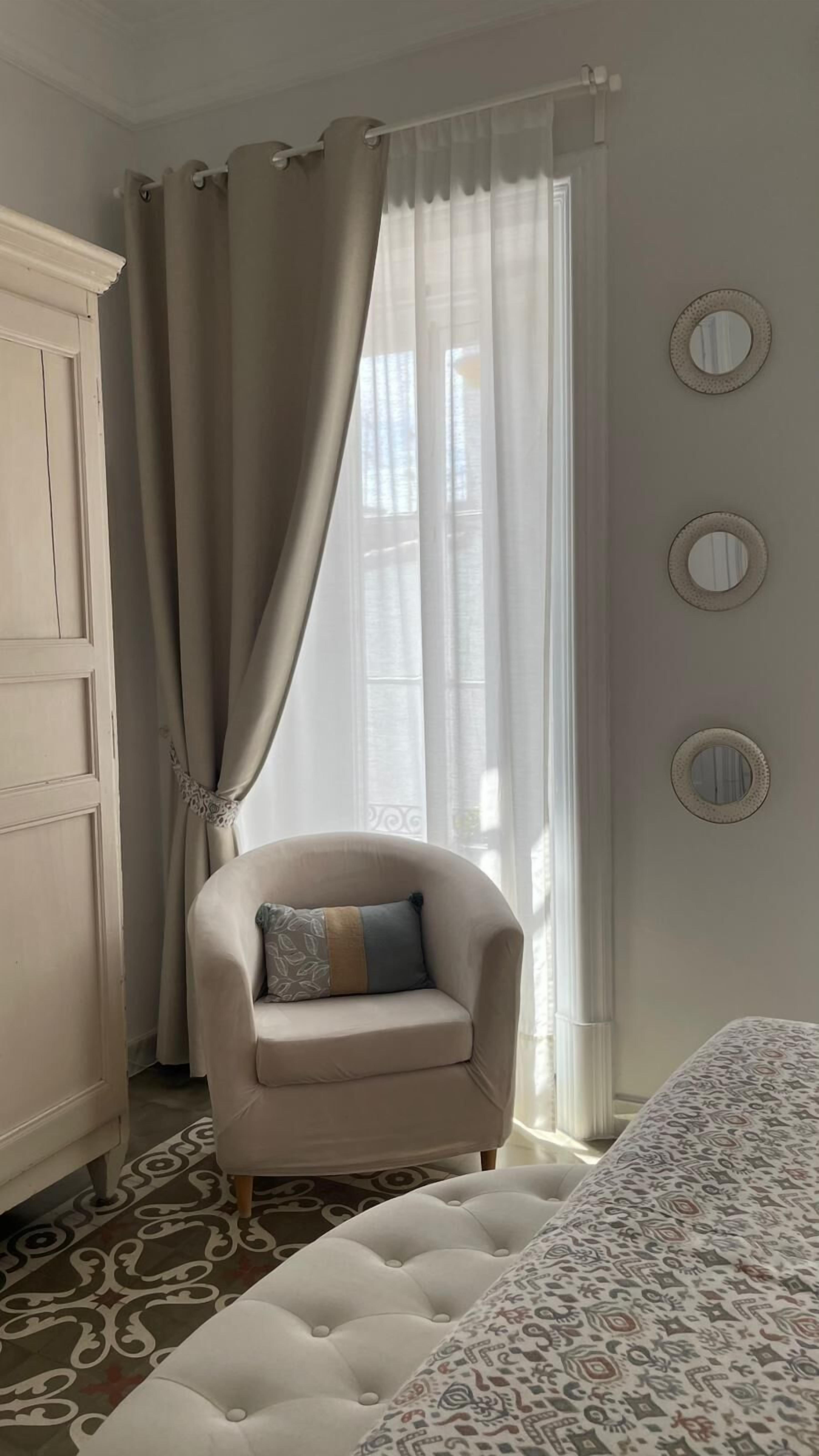 A room with a bed, a chair, a wardrobe, and a window with curtains.