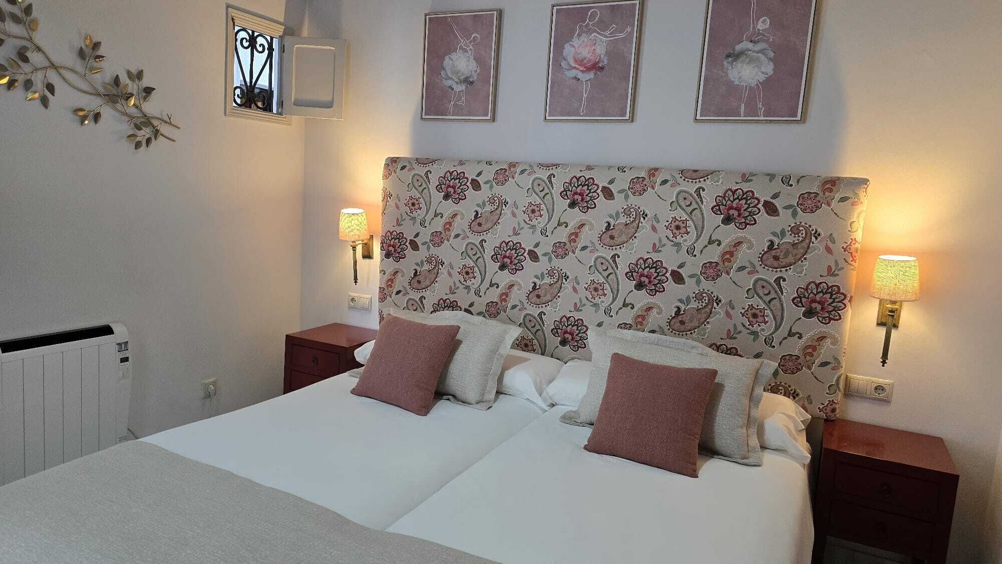 Ein ordentlich eingerichtetes Schlafzimmer mit einem blumengemusterten Kopfteil, zwei Nachttischlampen und einer Heizung.