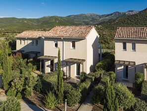 A residential area with modern houses, a paved driveway, and a mountainous backdrop. - Holiday Park in Corsica with Terrace Homes (Belgodere)