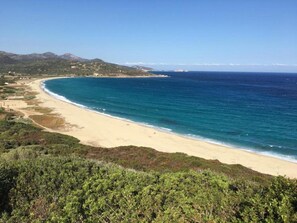 A coastal landscape with a sandy beach, clear blue sea, and green vegetation.