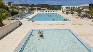 En pool med kristallklart vatten, omgiven av solstolar och parasoller, med kullar i bakgrunden.