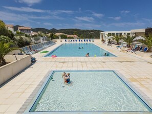 Ein Swimmingpool mit klarem Wasser, umgeben von Liegestühlen und Sonnenschirmen, mit Hügeln im Hintergrund.