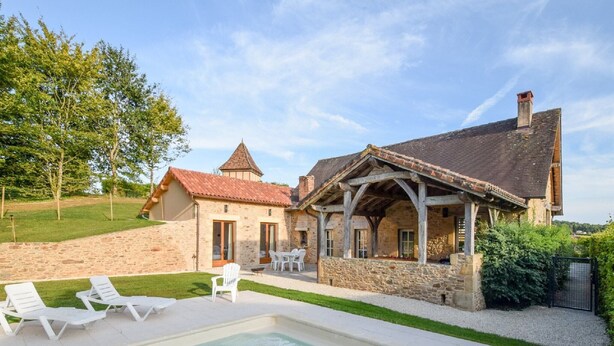A stone house with a swimming pool, outdoor seating, and a stone wall.