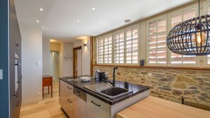 A modern kitchen with a stone backsplash, a large island with a sink, and a dining area with a wooden table.
