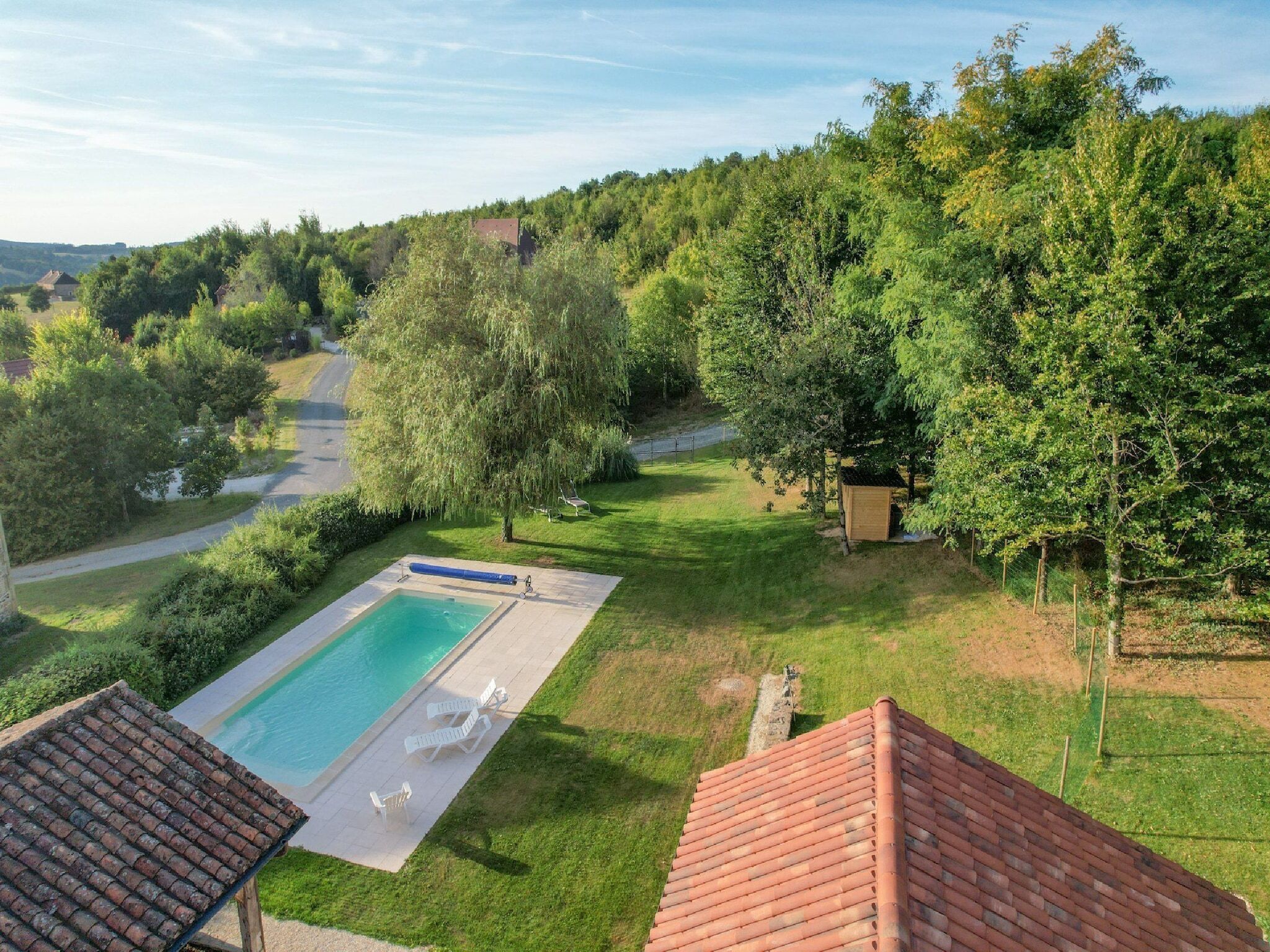 A swimming pool with a tiled deck, surrounded by grass and trees.