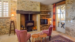 A cozy living room with stone walls, a fireplace, a television, and two pink chairs.