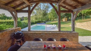 A wooden gazebo with a pool view, stone walls, and outdoor seating.