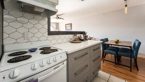 A modern kitchen with a white stove, hexagonal tile backsplash, and a dining area with blue chairs.