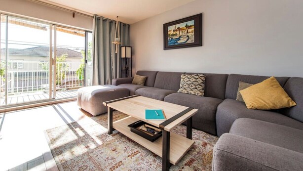 A modern living room with a grey sofa, a wooden coffee table, and a large sliding glass door leading to a balcony.
