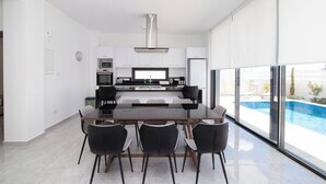 Une cuisine moderne dotée d’un îlot central, d’un coin repas avec une table en verre et d’une vue sur une piscine.