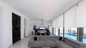Un salon moderne avec un grand canapé d’angle gris, une table basse en bois et une vue sur une piscine, visible à travers de grandes fenêtres.