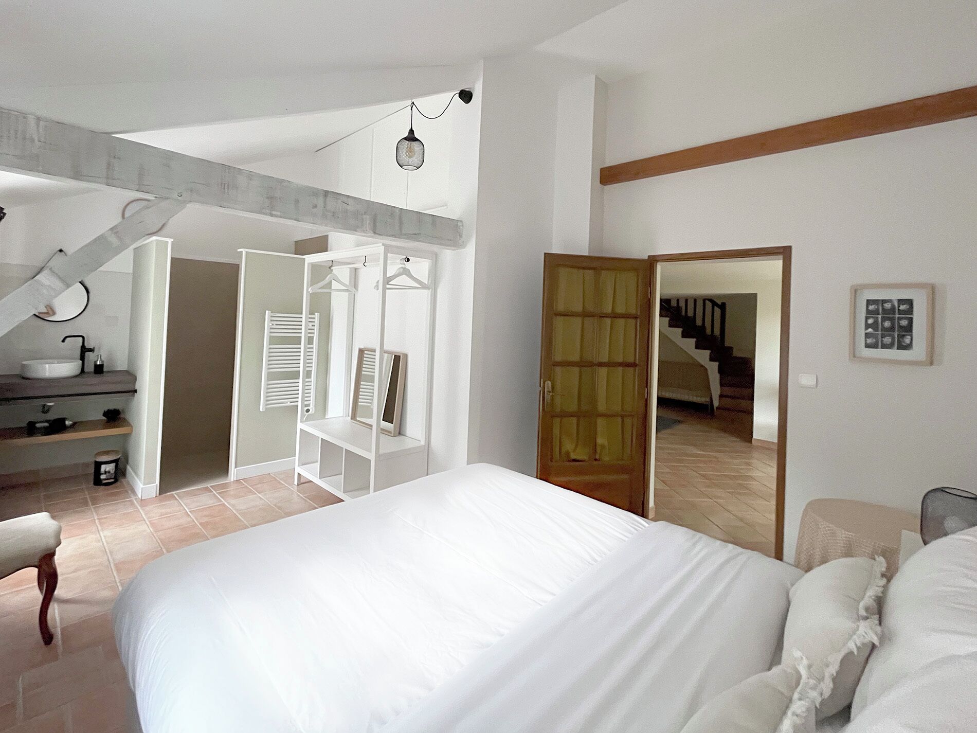 Une chambre avec un grand lit, un dressing, une salle de bain avec un lavabo et un escalier menant à un autre étage.