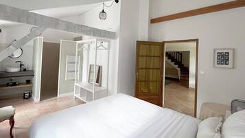 Une chambre avec un grand lit, un dressing, une salle de bain avec un lavabo et un escalier menant à un autre étage.