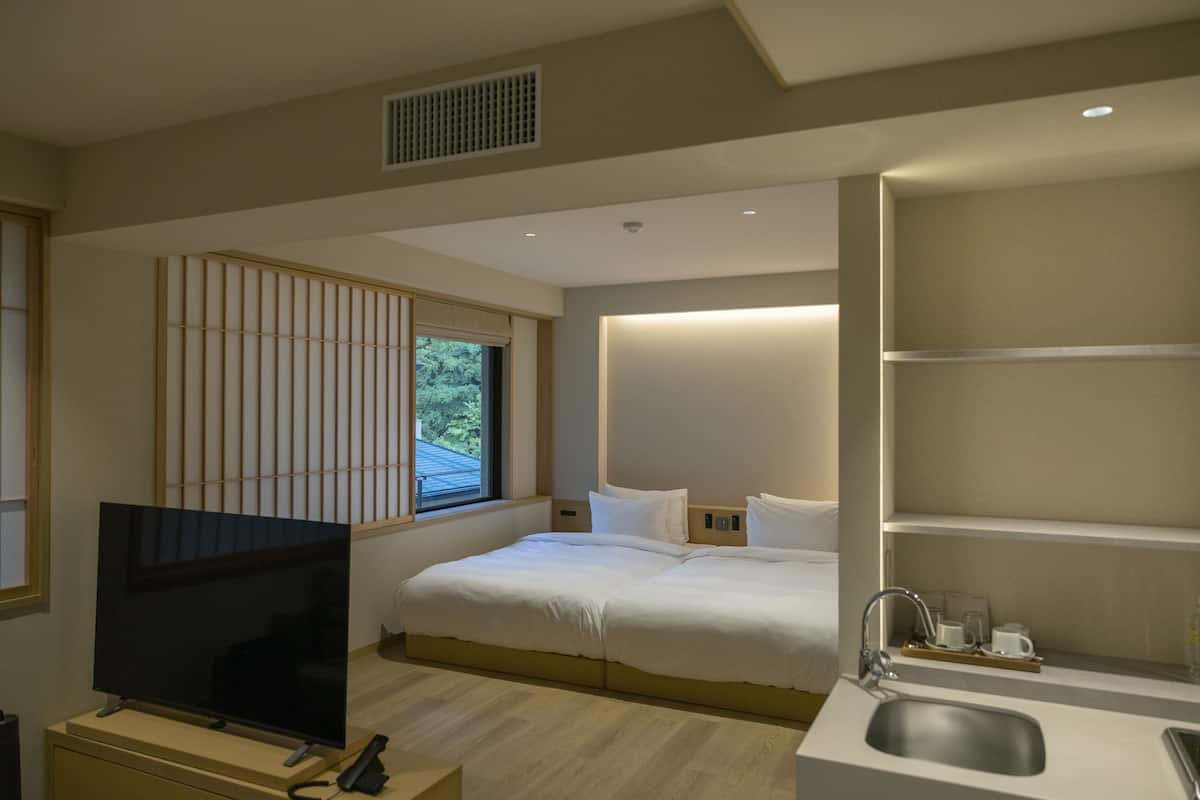 Ett modernt hotellrum med en stor säng, en TV, ett handfat och ett fönster med persienner.