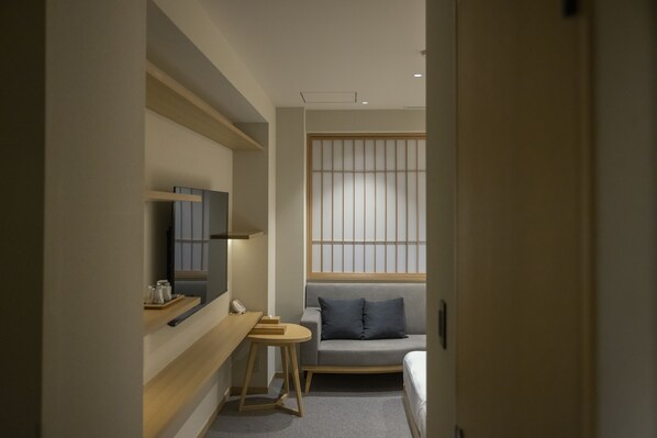 A small, modern hotel room with a sofa, a small table, a TV, and a sliding door.